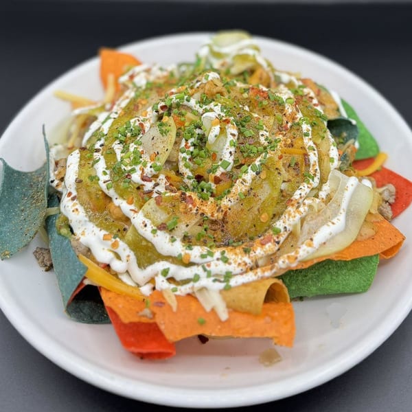 Colorful nachos with green chile, sour cream, chives, and spices on a white plate.