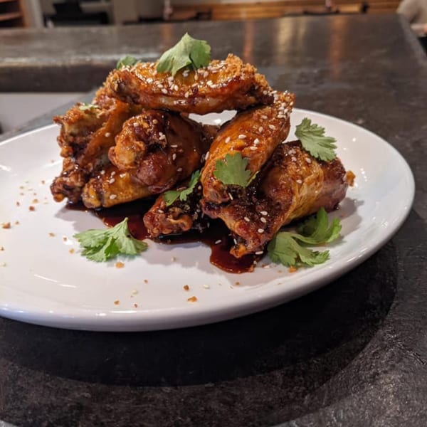 A plate of ForkLift Restaurant's southern-style chicken wings, glazed with sauce, sesame seeds, and cilantro.