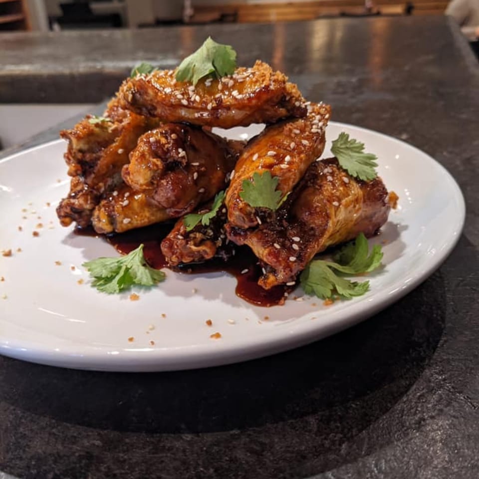 A plate of ForkLift Restaurant's southern-style chicken wings, glazed with sauce, sesame seeds, and cilantro.