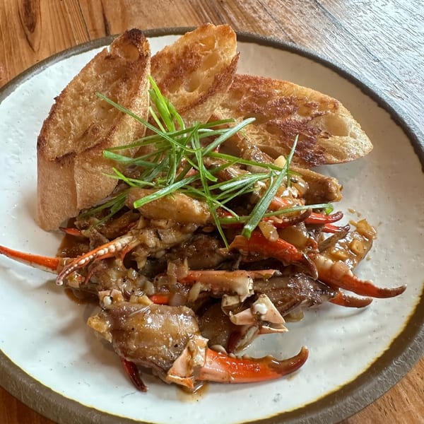 Southern-style crab claws in a rich sauce, garnished with green onions and served with toasted bread.