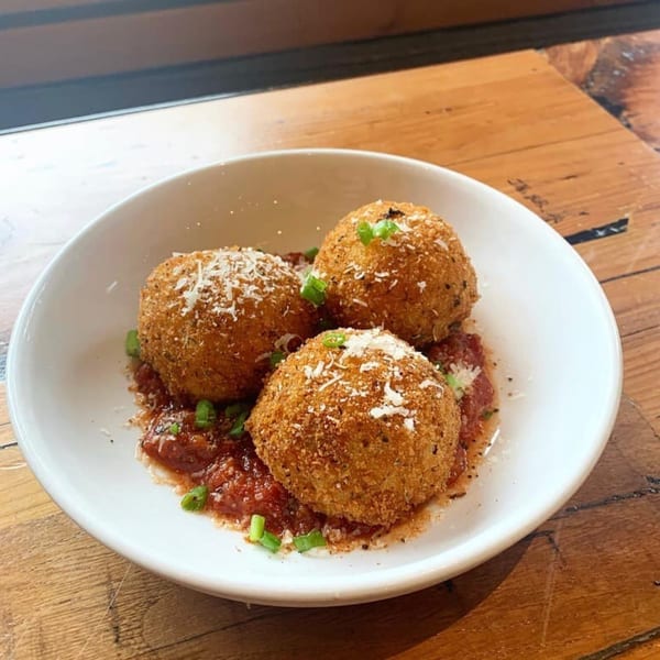 Three golden-brown arancini balls with marinara sauce, parmesan, and green onions in a white bowl.