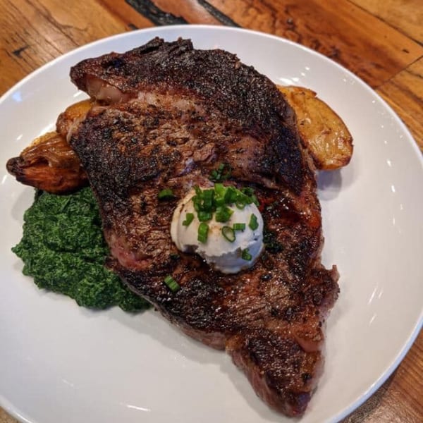 ForkLift Restaurant's southern-style steak with creamed spinach, roasted potatoes, and chives on a white plate.