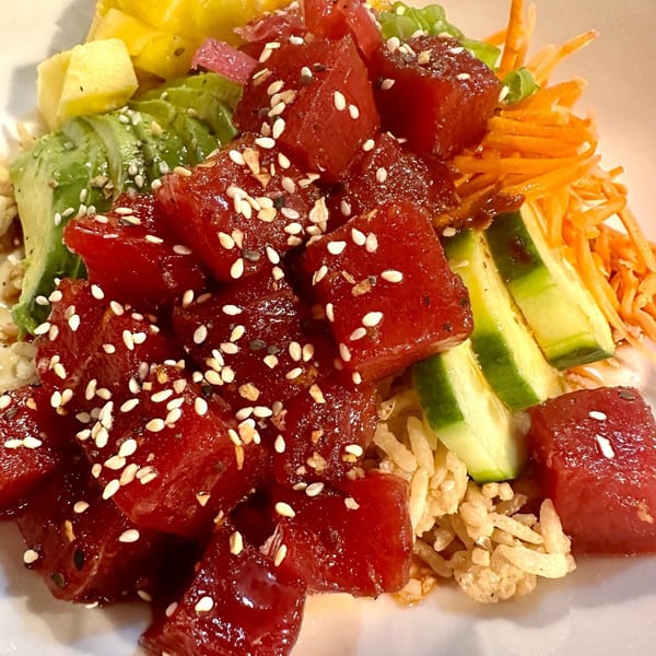 Close-up of a poke bowl with tuna, avocado, pineapple, cucumber, and shredded carrots.