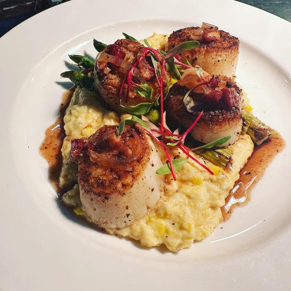 Seared scallops with asparagus, corn grits, and red onion relish on a white plate.