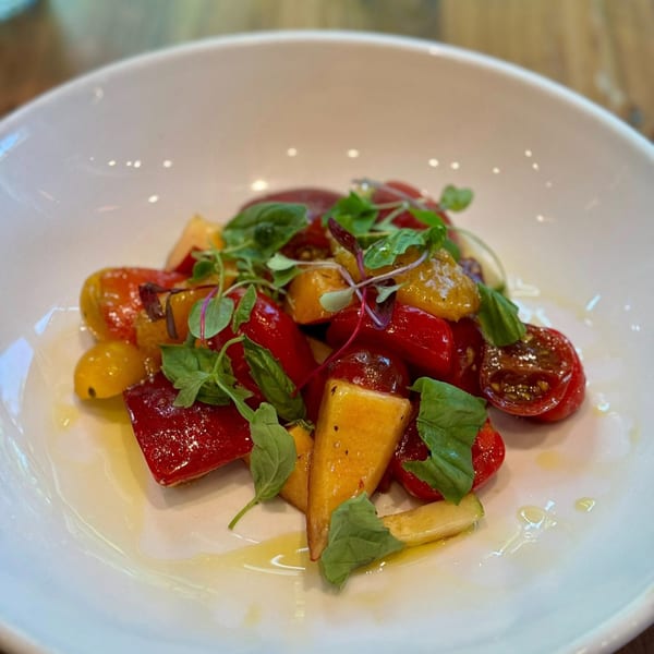 A vibrant salad with red and yellow tomatoes, green herbs, and a light dressing in a white bowl.