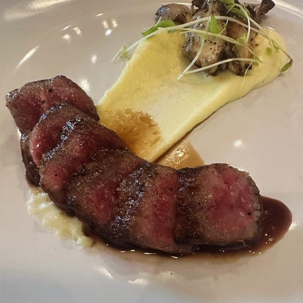Sliced steak with a side of creamy polenta, mushrooms, and microgreens on a white plate.