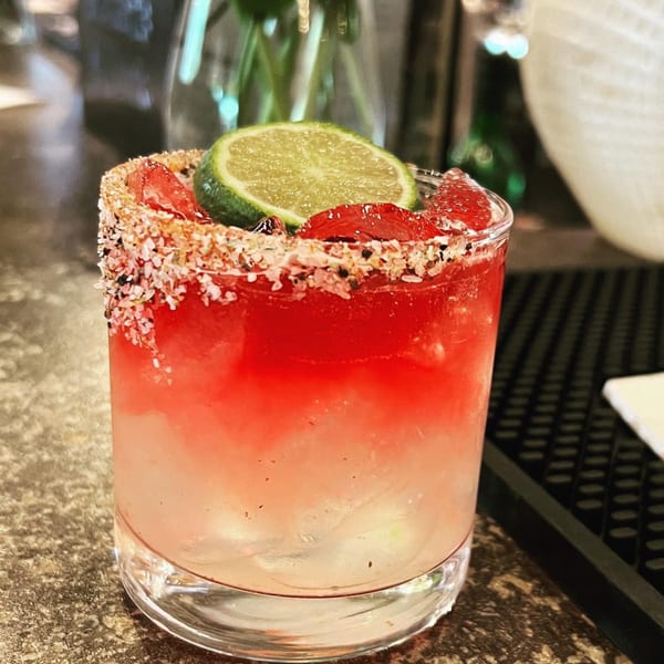 A vibrant red and white cocktail with a lime slice and a salt-rimmed glass.