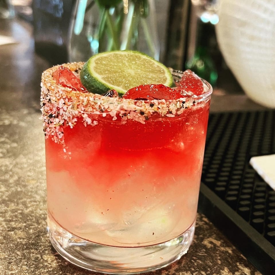 A vibrant red and white cocktail with a lime slice and a salt-rimmed glass.