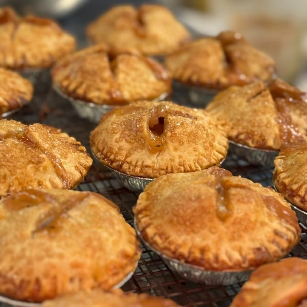 Close-up of several golden-brown mini fruit pies with flaky crusts on a cooling rack.