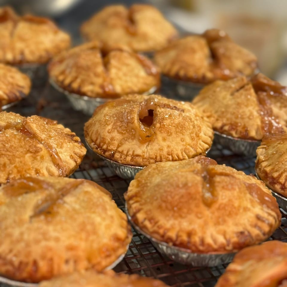 Close-up of several golden-brown mini fruit pies with flaky crusts on a cooling rack.
